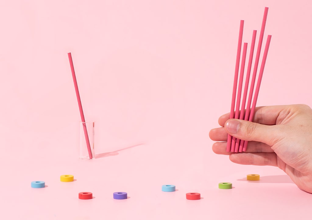 Game Shelf Stick Collection – ranka laiko rožinius pagaliukus, žaidimo elementai išdėstyti ant rožinio fono.