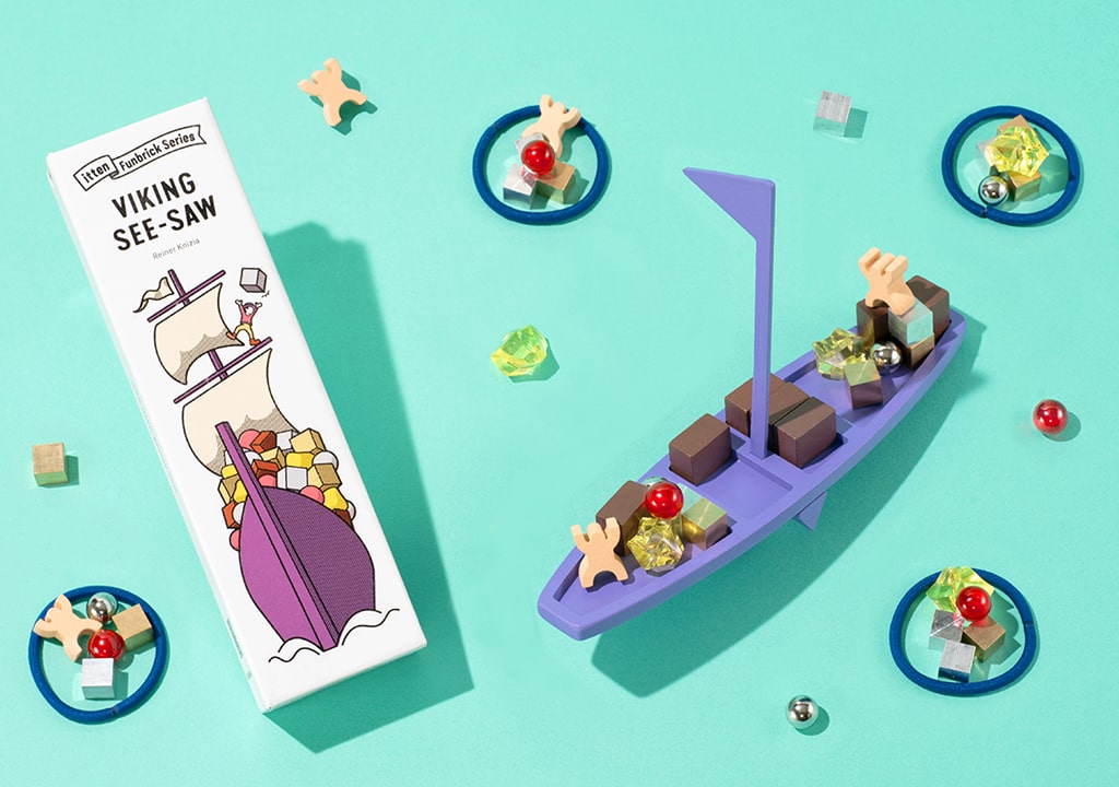 Game Shelf Viking See-Saw žaidimas – violetinis vikingo laivas su kroviniais, žaidimo dėžutė ir spalvoti elementai.